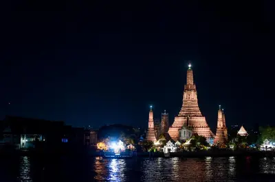 a lit up building next to the water at night at Arun Residence in Bangkok
