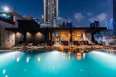 a swimming pool with chairs and a city at night at The Key Premier Hotel Sukhumvit Bangkok in Bangkok