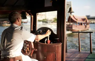 a man is sitting on a boat at The Peninsula Bangkok in Bangkok