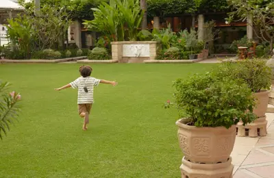 a young boy running on the grass in a garden at The Peninsula Bangkok in Bangkok