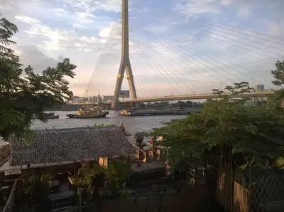a suspension bridge over a river with a building at New Phiman Riverview Guesthouse in Bangkok