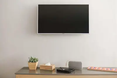 a television on a white wall with a desk with a plant at Kritthai Residence in Bangkok