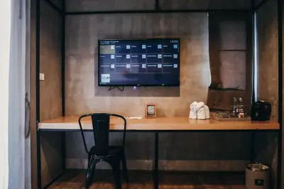 a desk with a monitor and a chair in a room at De Prime Rangnam Hotel in Bangkok