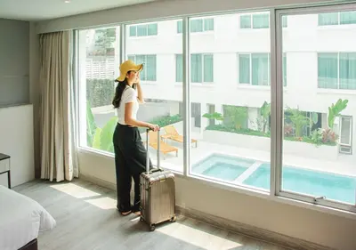 a woman in a hotel room with her luggage looking out the window at Centre Point Sukhumvit 10 in Bangkok