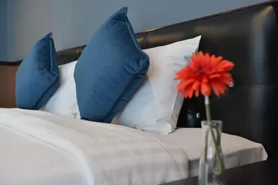 a vase with a red flower on a bed with pillows at The Breton Hotel Media in Bangkok