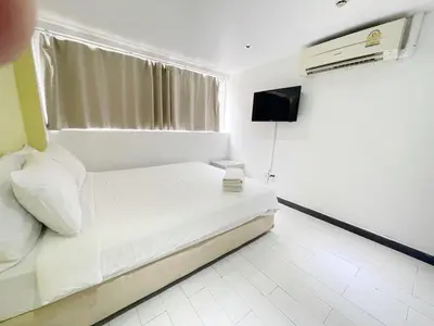 a white bedroom with a bed and a television at Nantra Ekkamai Hotel in Bangkok