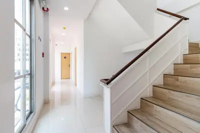 a hallway with white walls and wooden stairs at Atnest Hostel in Bangkok