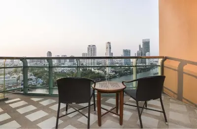 a balcony with two chairs and a table and a view at Chatrium Hotel Riverside Bangkok in Bangkok