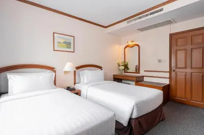 a hotel room with two beds and a mirror at Grand Diamond Suites Hotel in Bangkok
