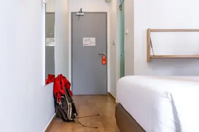 a room with a bed and a red backpack next to a door at Easy Planet Bangkok Asoke in Bangkok