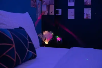 a dark room with a bed with a purple bedspread and a clock at Sleep with Me Bangkok - BTS Phra Khanong in Bangkok
