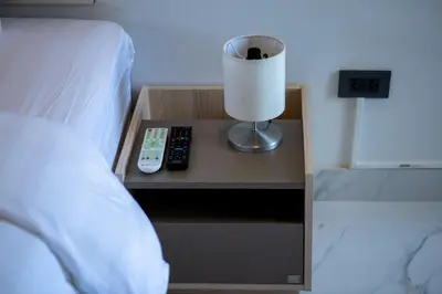 a bedside table with a lamp and remote controls on it at Rich8 Hostel in Bangkok