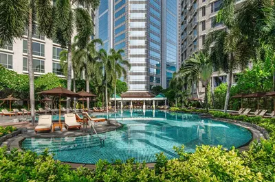 a swimming pool with chairs and palm trees and buildings at Conrad Bangkok Residences in Bangkok
