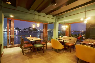 a restaurant with tables and chairs and a view of the water at Baan Wanglang Riverside, Bangkok in Bangkok