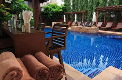 a pool with a table and a chair next to a swimming pool at Rose Hotel in Bangkok