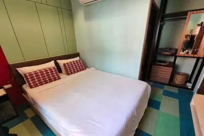 a small bedroom with a white bed with two pillows at Lilliput Riverside Bangkachao in Samutprakarn