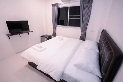 a bedroom with a bed with white sheets and a television at U-need Guesthouse95 in Bangkok