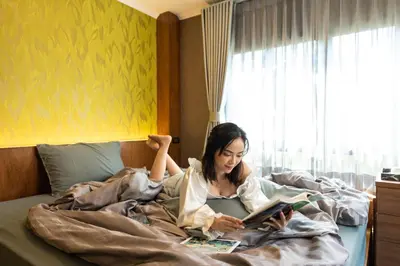 a woman laying in bed reading a book at Tepbunthom Hostel in Bangkok
