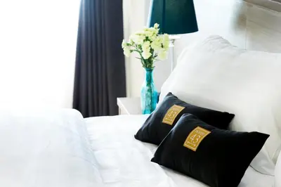 a white bed with black pillows and a vase with flowers at Poste 43 Residence in Bangkok