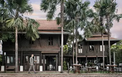 a man walking in front of a building with palm trees at The Siam in Bangkok