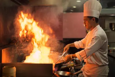 a chef cooking on a grill with flames at The Berkeley Hotel Pratunam in Bangkok