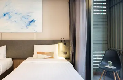 a bedroom with a bed and a chair next to a window at SOVA Hotel Bangkok in Bangkok