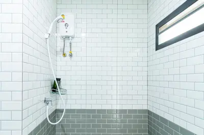 a shower in a bathroom with white tiles at BeWish Residence Bangphlat in Bangkok