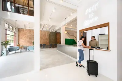 a man with a suitcase standing at a counter in an office at REST IS MORE hostel in Bangkok