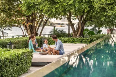 a family sitting on a couch next to a swimming pool at Four Seasons Hotel Bangkok at Chao Phraya River in Bangkok