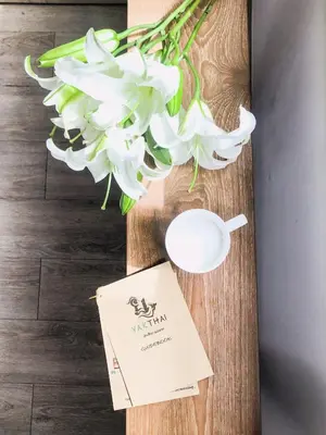 a table with a vase of white flowers and a card at YAKTHAI POSHTEL in Bangkok