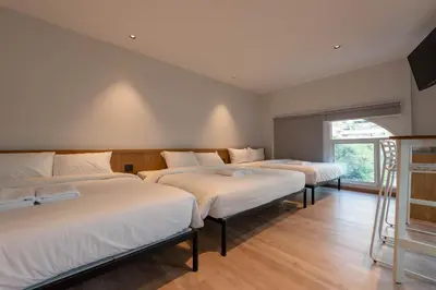 three beds in a room with white sheets and a window at Boxpackers Pratunam in Bangkok