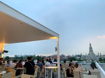 people sitting at tables on a balcony with a view of the city at ARUN Riverside Bangkok in Bangkok