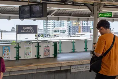 a man looking at his cell phone at a train station at U2 Large 2 Bedrooms 100m to BTS station in Bangkok