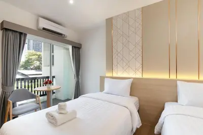 a hotel room with two beds and a chair at Riski Residence Ngamwongwan in Nonthaburi