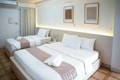 two beds in a hotel room with white sheets at ปลื้มจิต อพาร์ทเม้น บางใหญ่ in Nonthaburi