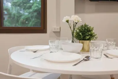 a white table with plates and glasses and a vase with flowers at S3 Silom26 · S3 Silom central, large room, full kitchen, WIFI, in Bangkok