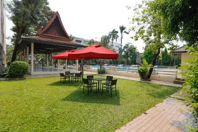 a table and chairs with a red umbrella in the grass at D-haus Ladprao Residence in Bangkok