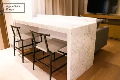 a white marble counter with two chairs and a tv at ashley hotel bkk in Bangkok
