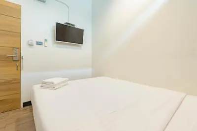 a bedroom with a white bed with a television on the wall at T Hostel @ Victory Monument in Bangkok