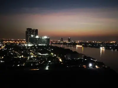 a city lit up at night with a river and buildings at river front in Nonthaburi