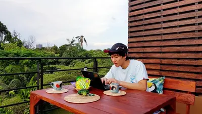 a young man sitting at a table with a laptop at BaanSuanklaiKlungBangkrachao บ้านสวนใกล้กรุงบางกะเจ้า in Phra Pradaeng