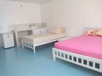a room with two beds and a bench and a table at Thailand Taxiapartment Hostel in Thung Si Kan