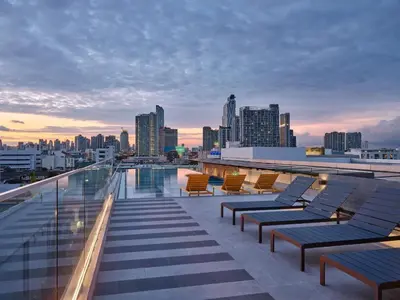 a rooftop deck with lounge chairs and a city skyline at The Quarter Onnut by UHG in Bangkok
