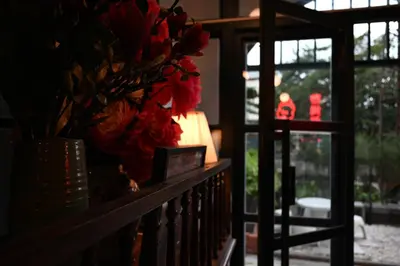 a table with a vase of red flowers and a window at Tim Mansion in Bangkok