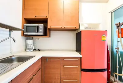 a small kitchen with wooden cabinets and a red refrigerator at Rama9 Cozy Apartment in Bangkok