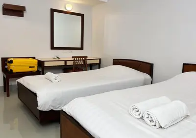 two beds in a room with a desk and a mirror at Niagara Hotel in Bangkok