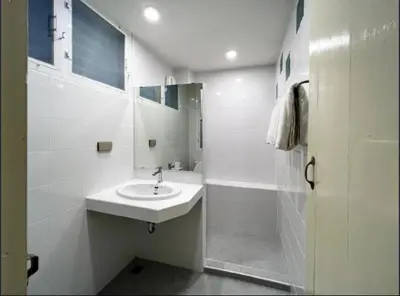 a white bathroom with a sink and a shower at Niagara Hotel in Bangkok