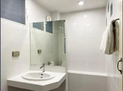 a white bathroom with a sink and a mirror at Niagara Hotel in Bangkok