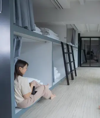a woman sitting on the floor in a bunk bed at 3Howw Hostel @ Sukhumvit 21 in Bangkok