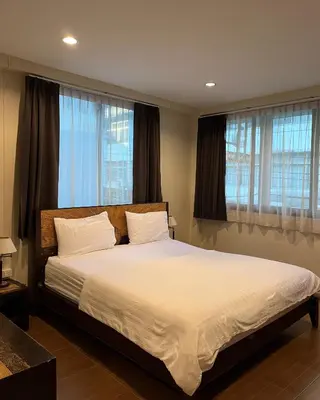 a bedroom with a bed with white sheets and windows at Baan Glang Soi Restaurant & Guesthouse in Bangkok